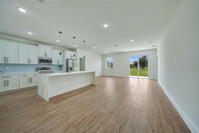 kitchen with white cabinets, light wood-type flooring, stainless steel appliances, an island with sink, and pendant lighting