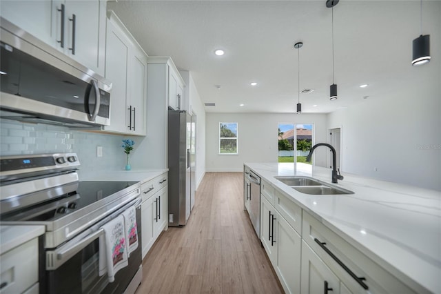 kitchen with pendant lighting, white cabinetry, light hardwood / wood-style flooring, stainless steel appliances, and sink