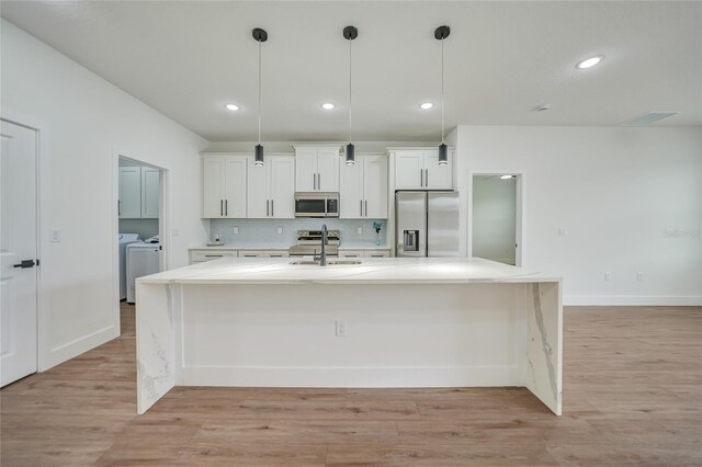 kitchen featuring light wood-type flooring, appliances with stainless steel finishes, an island with sink, and washer and clothes dryer