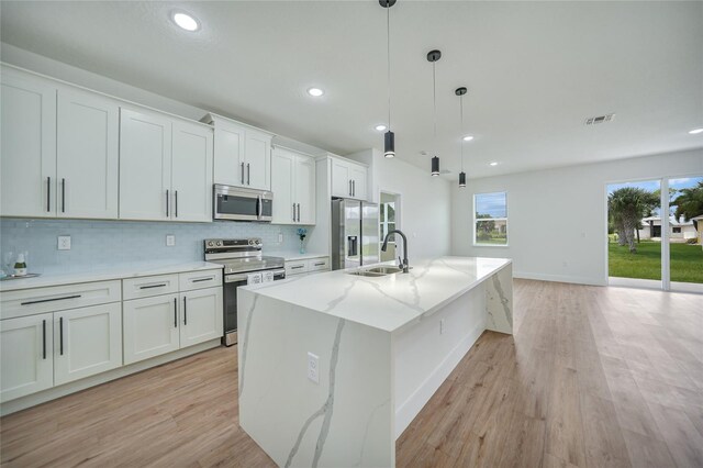 kitchen with a kitchen island with sink, light wood-type flooring, sink, appliances with stainless steel finishes, and white cabinets