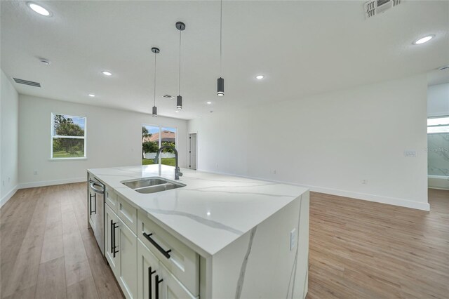 kitchen featuring hanging light fixtures, light wood-type flooring, light stone countertops, sink, and a center island with sink