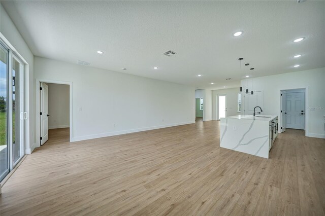 unfurnished living room featuring light wood-type flooring, a textured ceiling, and sink