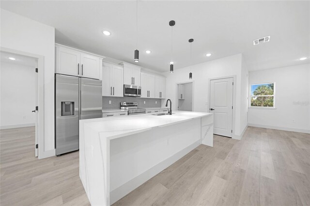 kitchen with an island with sink, light hardwood / wood-style flooring, stainless steel appliances, and white cabinets