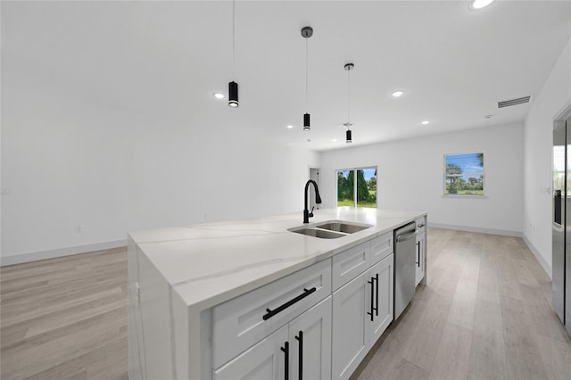 kitchen featuring stainless steel dishwasher, light stone countertops, light wood finished floors, and a sink