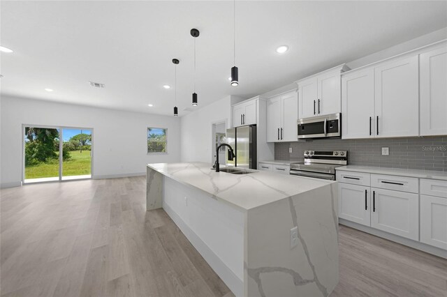 kitchen with light wood-type flooring, an island with sink, light stone countertops, appliances with stainless steel finishes, and white cabinets