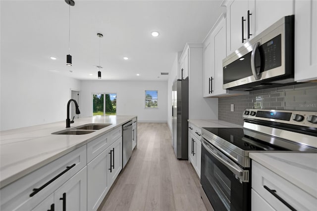 kitchen with a sink, tasteful backsplash, white cabinetry, stainless steel appliances, and light wood-style floors