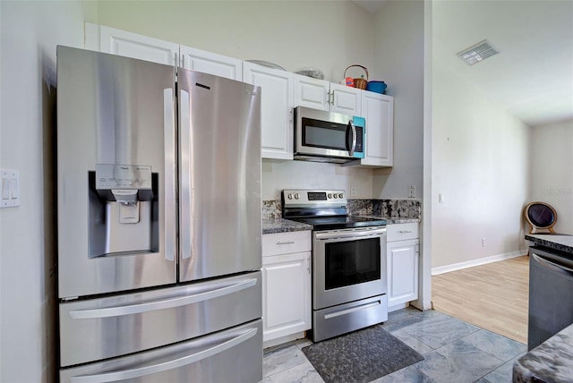 kitchen featuring dark stone counters, appliances with stainless steel finishes, light hardwood / wood-style flooring, and white cabinets