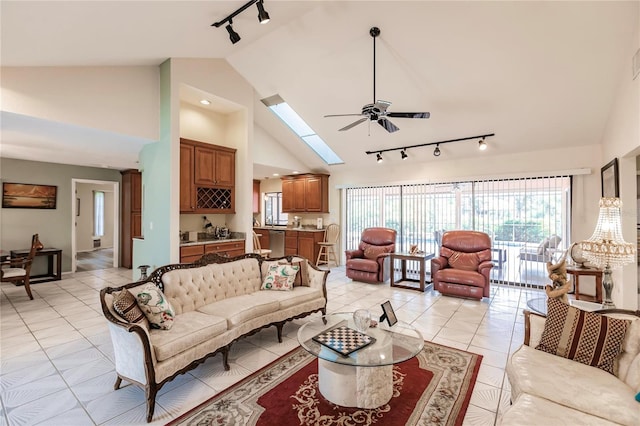 tiled living room with high vaulted ceiling, ceiling fan, a skylight, and track lighting