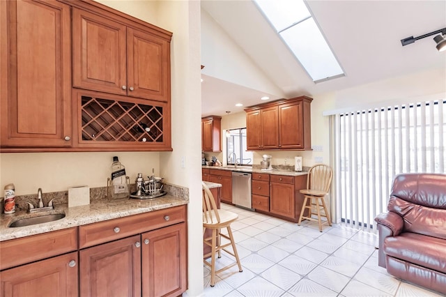 kitchen featuring dishwasher, light stone countertops, sink, and lofted ceiling with skylight