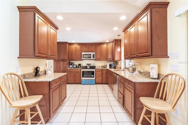 kitchen featuring a breakfast bar, stainless steel appliances, light stone counters, and decorative light fixtures