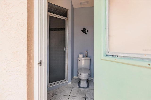 bathroom featuring toilet, a shower with door, and tile patterned floors