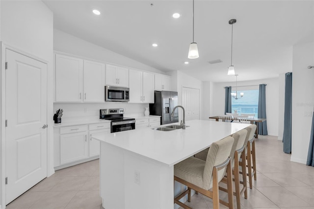 kitchen featuring an island with sink, lofted ceiling, hanging light fixtures, sink, and appliances with stainless steel finishes