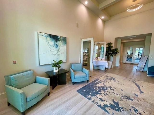 sitting room with wood-type flooring, beamed ceiling, french doors, and a high ceiling