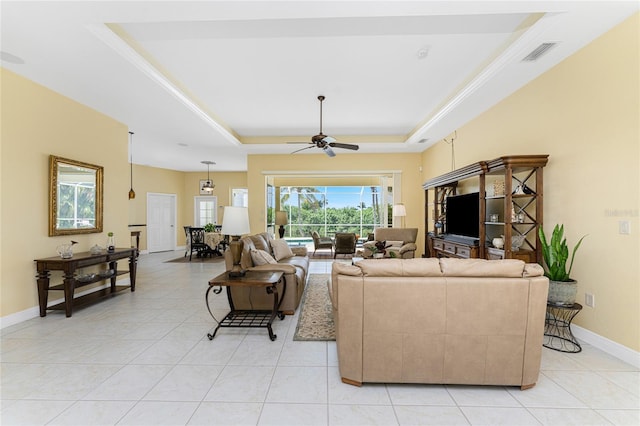 tiled living room with ceiling fan and a tray ceiling