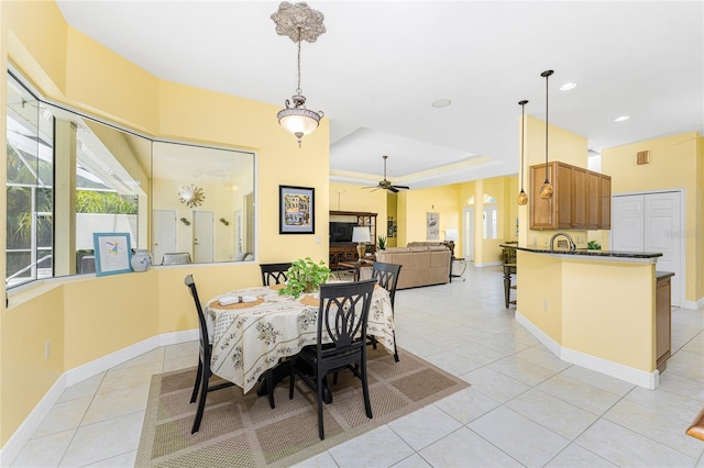 dining area featuring ceiling fan, sink, light tile patterned floors, and a tray ceiling