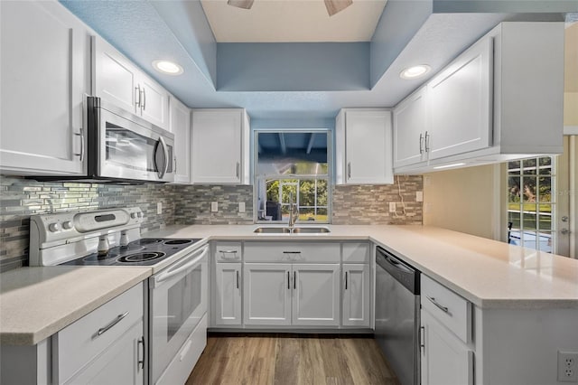 kitchen with kitchen peninsula, sink, appliances with stainless steel finishes, and white cabinetry