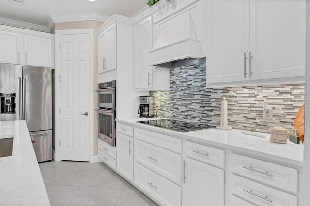 kitchen with white cabinets, light tile patterned floors, custom range hood, appliances with stainless steel finishes, and tasteful backsplash