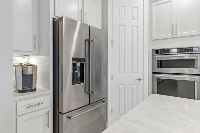 kitchen with appliances with stainless steel finishes, light stone counters, and white cabinetry