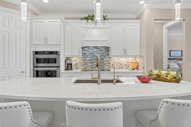 kitchen featuring white cabinets, decorative light fixtures, custom exhaust hood, stainless steel appliances, and a breakfast bar area