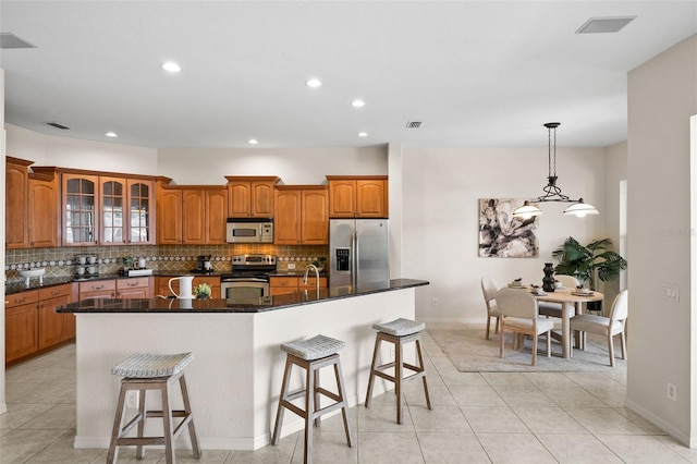 kitchen featuring a kitchen island with sink, pendant lighting, dark stone counters, a kitchen bar, and stainless steel appliances