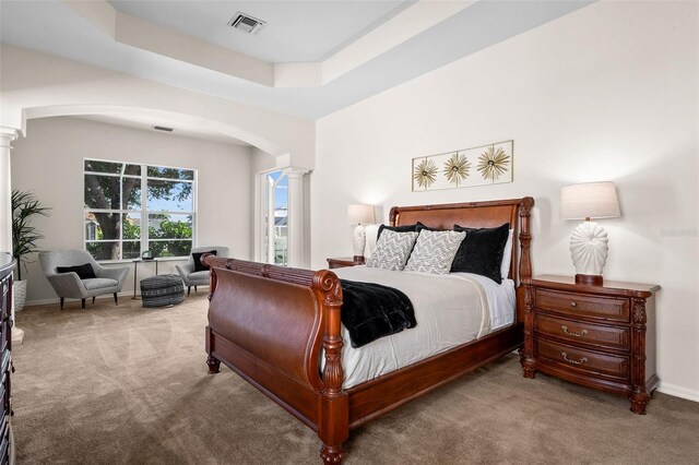 bedroom featuring a tray ceiling, decorative columns, and light carpet