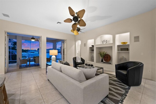 living room with built in features, light tile patterned flooring, and ceiling fan