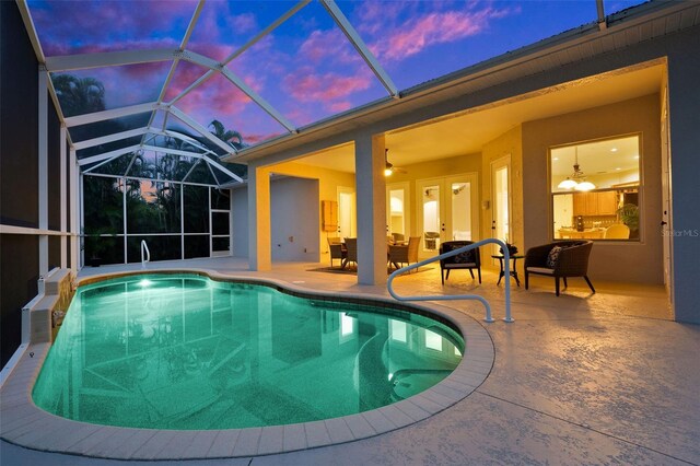 pool at dusk with a lanai, ceiling fan, an outdoor living space, and a patio area