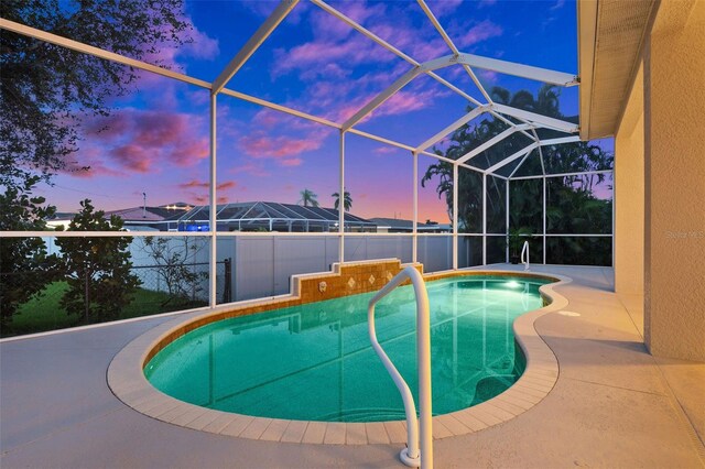 pool at dusk featuring glass enclosure and a patio area