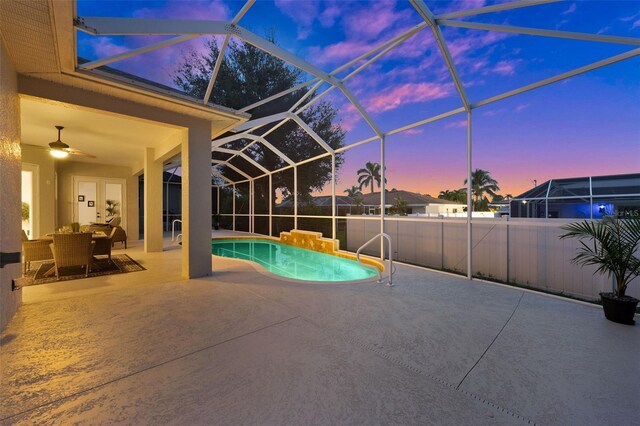 pool at dusk with a lanai, ceiling fan, and a patio area