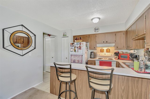 kitchen with white appliances, a textured ceiling, a kitchen bar, light tile patterned floors, and kitchen peninsula