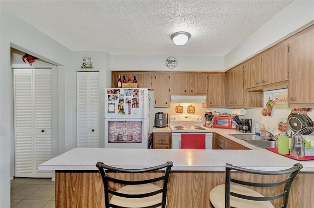 kitchen featuring a textured ceiling, white appliances, a breakfast bar, kitchen peninsula, and sink