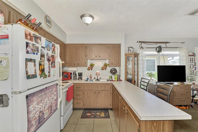 kitchen with white appliances, sink, kitchen peninsula, a kitchen bar, and a textured ceiling