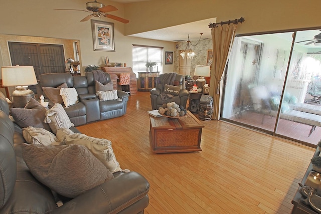 living room featuring ceiling fan with notable chandelier, a brick fireplace, and light hardwood / wood-style floors