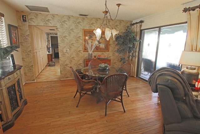 dining area with a textured ceiling, a notable chandelier, and light wood-type flooring