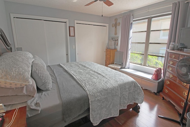 bedroom with a textured ceiling, ceiling fan, hardwood / wood-style floors, and multiple closets