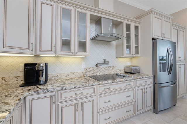 kitchen featuring wall chimney exhaust hood, decorative backsplash, light stone countertops, and stainless steel fridge