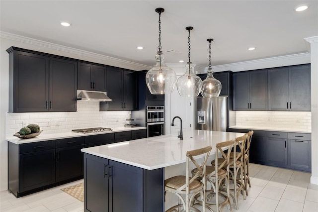 kitchen featuring an island with sink, stainless steel appliances, sink, crown molding, and decorative light fixtures