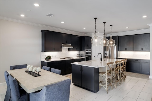 kitchen featuring appliances with stainless steel finishes, an island with sink, a kitchen bar, decorative light fixtures, and decorative backsplash