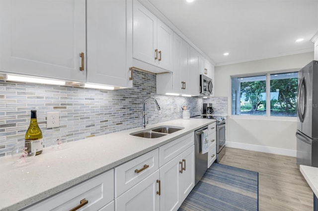 kitchen with appliances with stainless steel finishes, tasteful backsplash, sink, white cabinetry, and light wood-type flooring