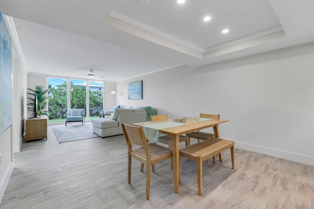 dining space with crown molding, a raised ceiling, and light wood-type flooring