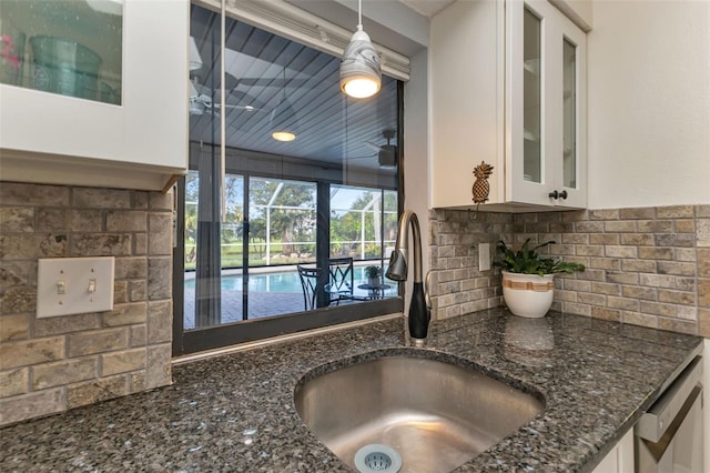 kitchen with dark stone countertops, white cabinetry, dishwasher, sink, and hanging light fixtures