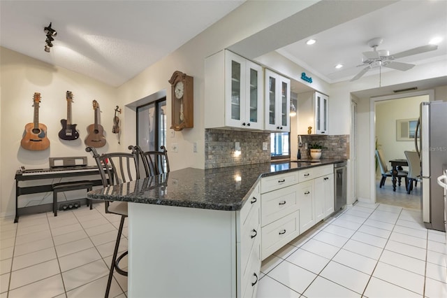 kitchen with stainless steel refrigerator, backsplash, a kitchen bar, ceiling fan, and white cabinets