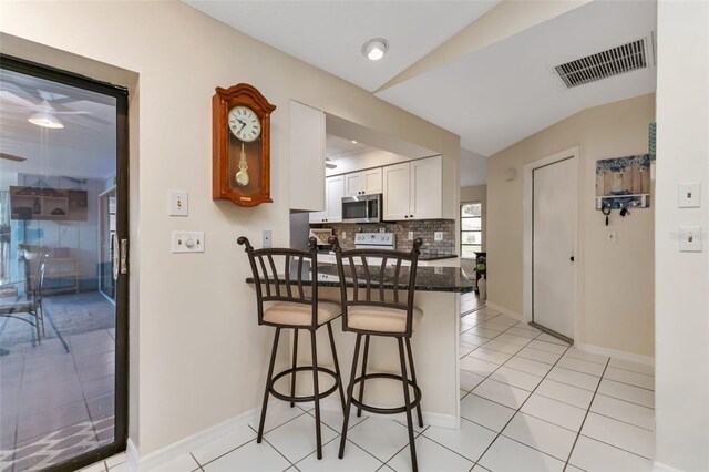 kitchen with vaulted ceiling, a kitchen breakfast bar, tasteful backsplash, dark stone countertops, and white cabinets