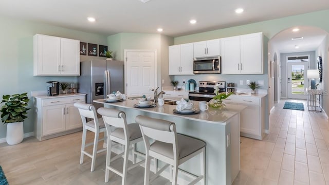 kitchen with stainless steel appliances, a kitchen breakfast bar, white cabinetry, and an island with sink