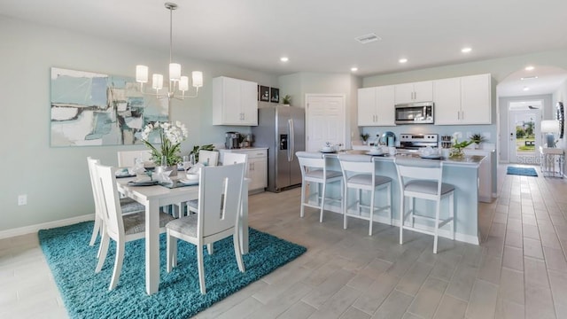 kitchen featuring a kitchen island with sink, white cabinets, decorative light fixtures, and stainless steel appliances