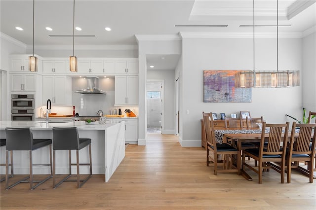 kitchen featuring light hardwood / wood-style floors, white cabinetry, decorative light fixtures, and wall chimney range hood