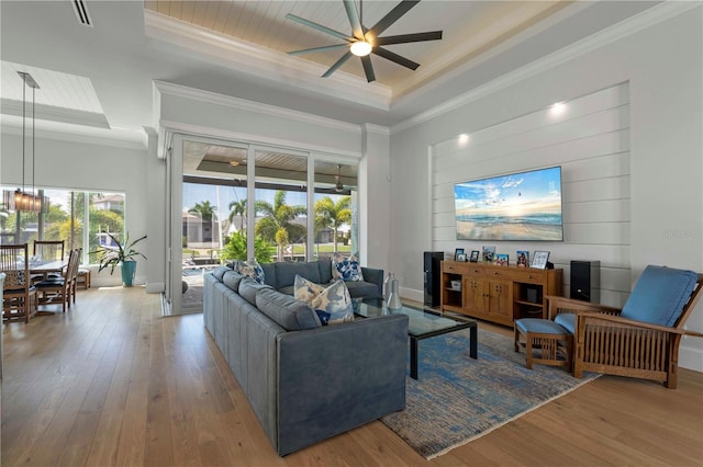 living room with a raised ceiling, wood-type flooring, and ceiling fan