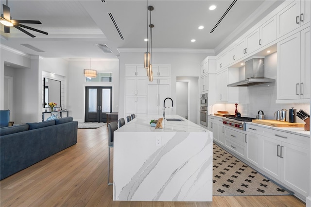 kitchen with light wood-type flooring, light stone countertops, wall chimney range hood, ceiling fan, and a kitchen bar