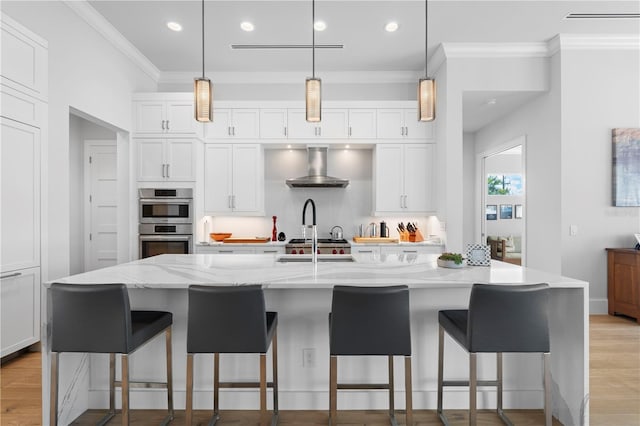 kitchen with an island with sink, light stone counters, wall chimney exhaust hood, and white cabinets