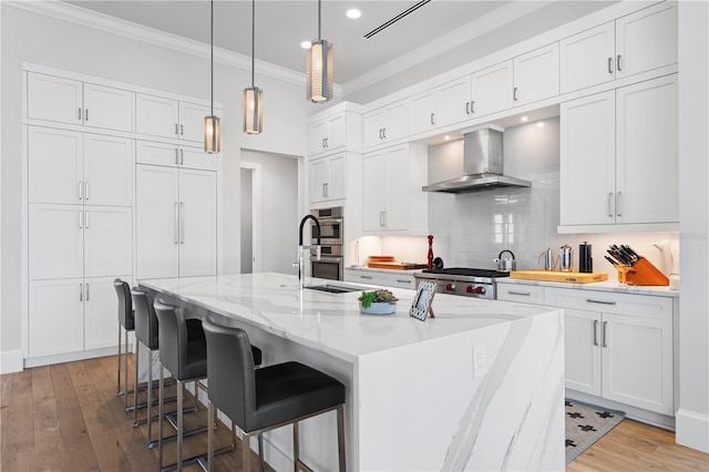 kitchen with an island with sink, light hardwood / wood-style flooring, wall chimney range hood, and a kitchen bar